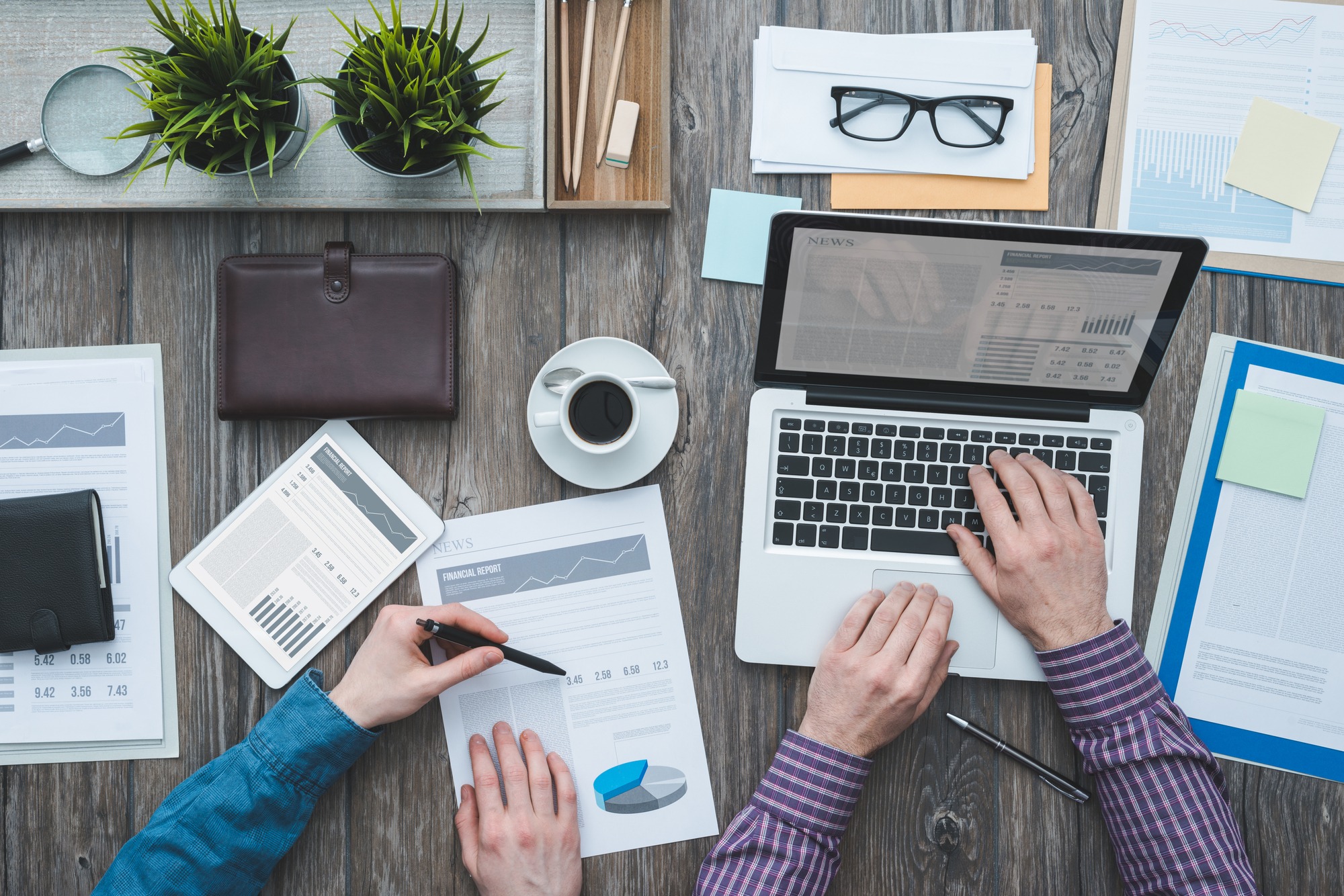 Business partners working together at office desk they are using a laptop and checking financial reports top view